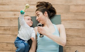 Top view of mother with baby boy lying on floor and playing with dumbbells