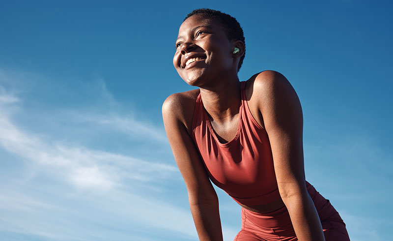 Blue sky in background, foreground black woman and happy athlete smiling after exercise. 